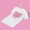 Funny and bold white t-shirt for Latina women with the phrase 'be kind chingona', with the word 'kind' crossed out, in a pink heart graphic and old-English style lettering