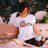 Latina wearing a white t-shirt for Latinas, featuring a humorous and empowering logo that says 'Chingona', parodying a famous rock-band logo