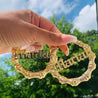 Latina woman holding Gold Personalized bamboo hoop earrings with custom name in old English font