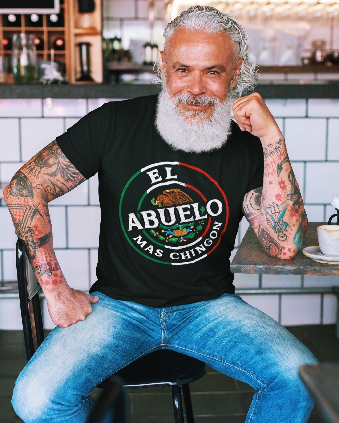 older mexican man wearing Cool 'El Abuelo Mas Chingon' T-Shirt for grandfathers in black with white text and a unique emblem in the Mexican colors and coat of arms