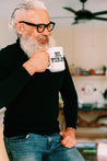 older hispanic man with white beard drinking from a tall white mug displaying the text "el viejo" in bold lettering