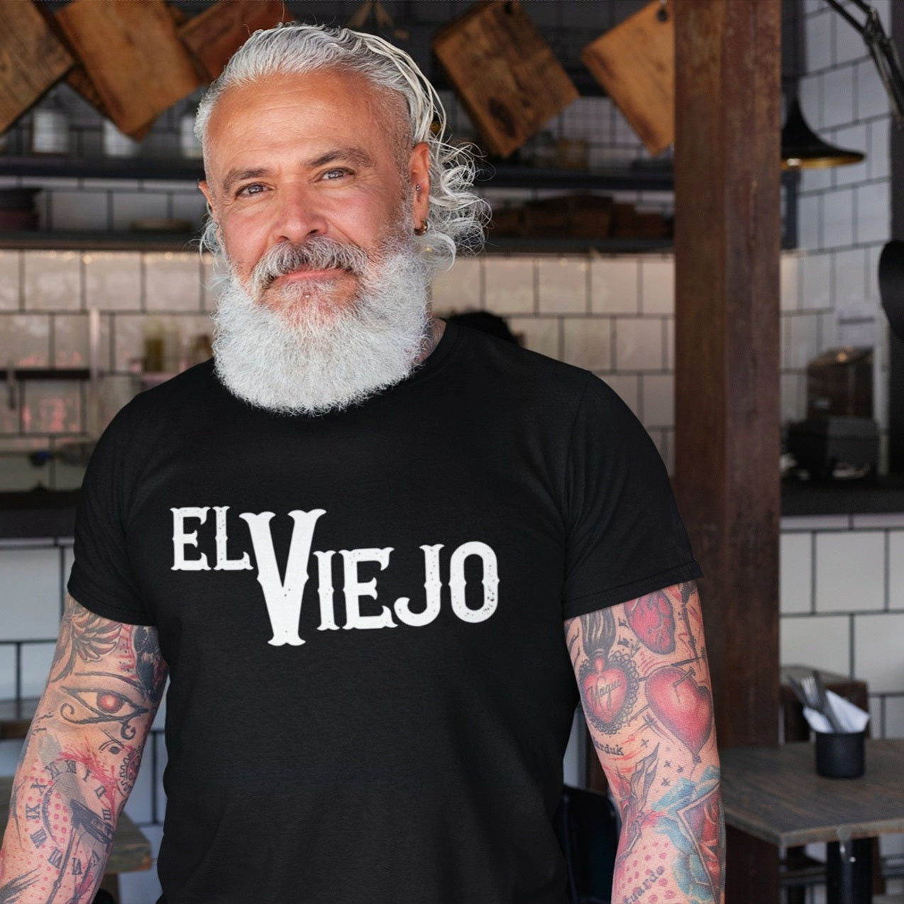 Older hispanic man wearing a funny black t-shirt for Latinos and Spanish-speakers. in bold white lettering, the front of the shirt states "El Viejo"