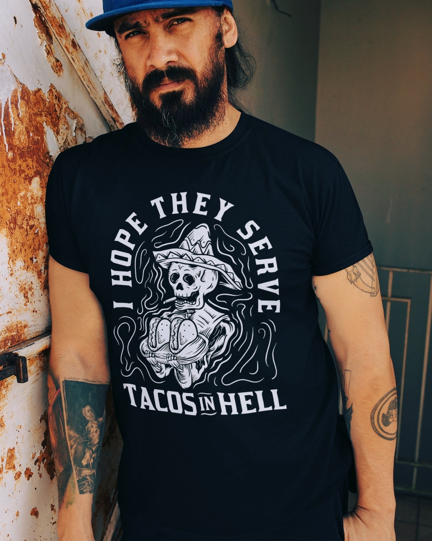 latino wearing a Funny t-shirt with a tattoo-style cartoon of a skeleton serving tacos and smoking, captioned 'I hope they serve tacos in hell.'
