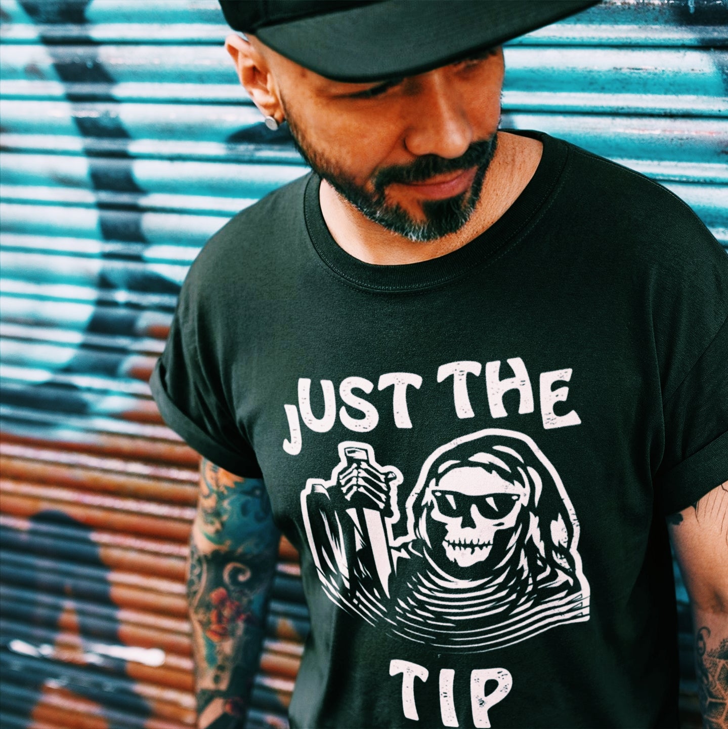 Mexican man wearing a funny black t-shirt for Latino men. The graphic is a humorous play on words. There is a tattoo-style skeleton holding a knife, and the words surrounding the image state "Just the Tip"