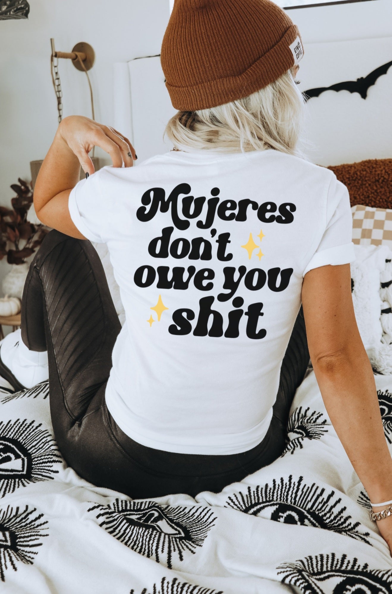 Mexican woman wearing an empowering white t-shirt for Hispanic women and Spanish-speakers. the printing on the back of the t-shirt states "Mujeres don't owe you shit" in bold black writing