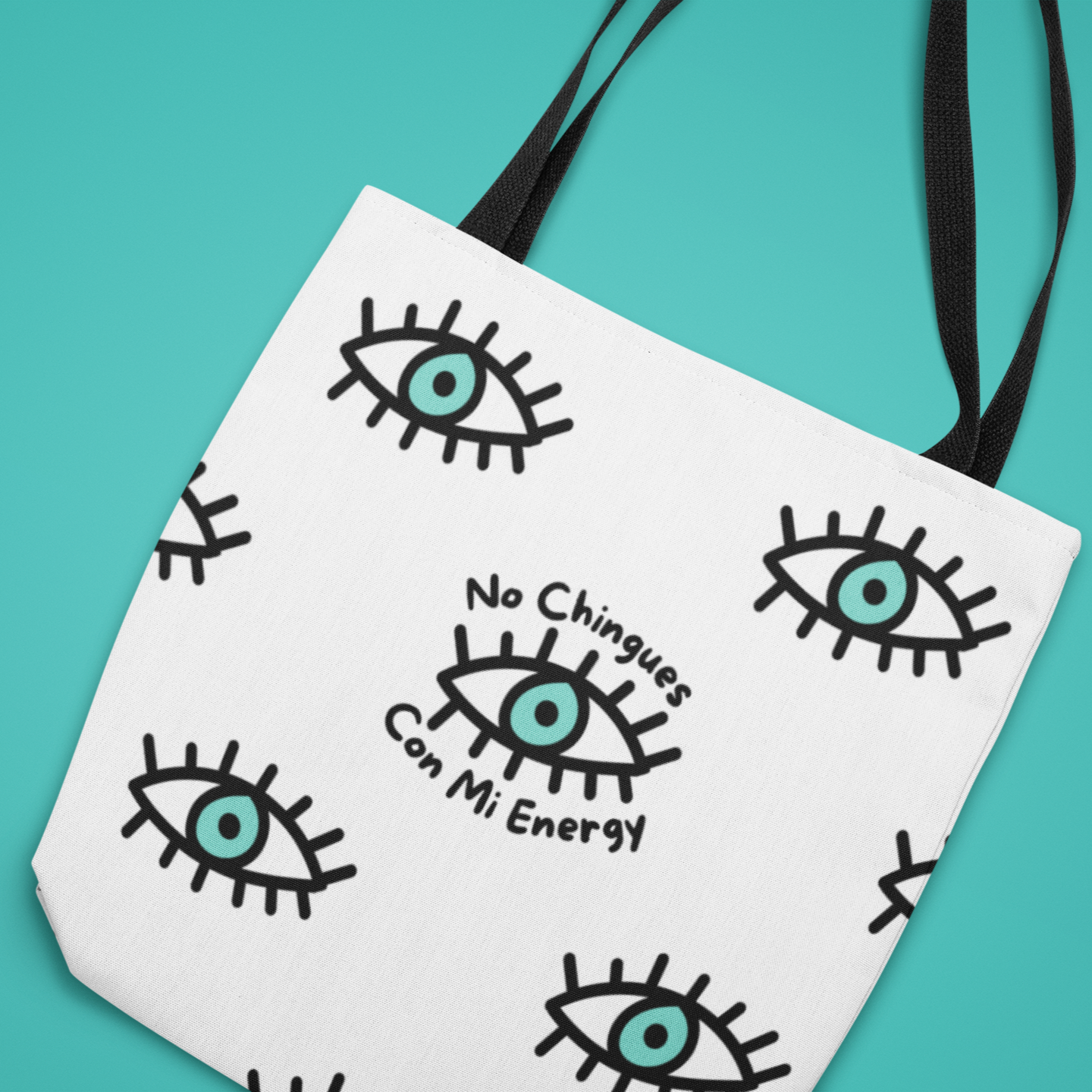 Angled view of a Latina-inspired large tote bag to celebrate Latino culture. The background is white and the graphic is evil eye themed in a repeating pattern with the phrase "no chingues con mi energy". Tote bag for Spanish speakers