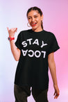 Latina woman wearing a black t-shirt with white 'Stay Loca' design, featuring 'Stay' in an arch and 'Loca' upside down
