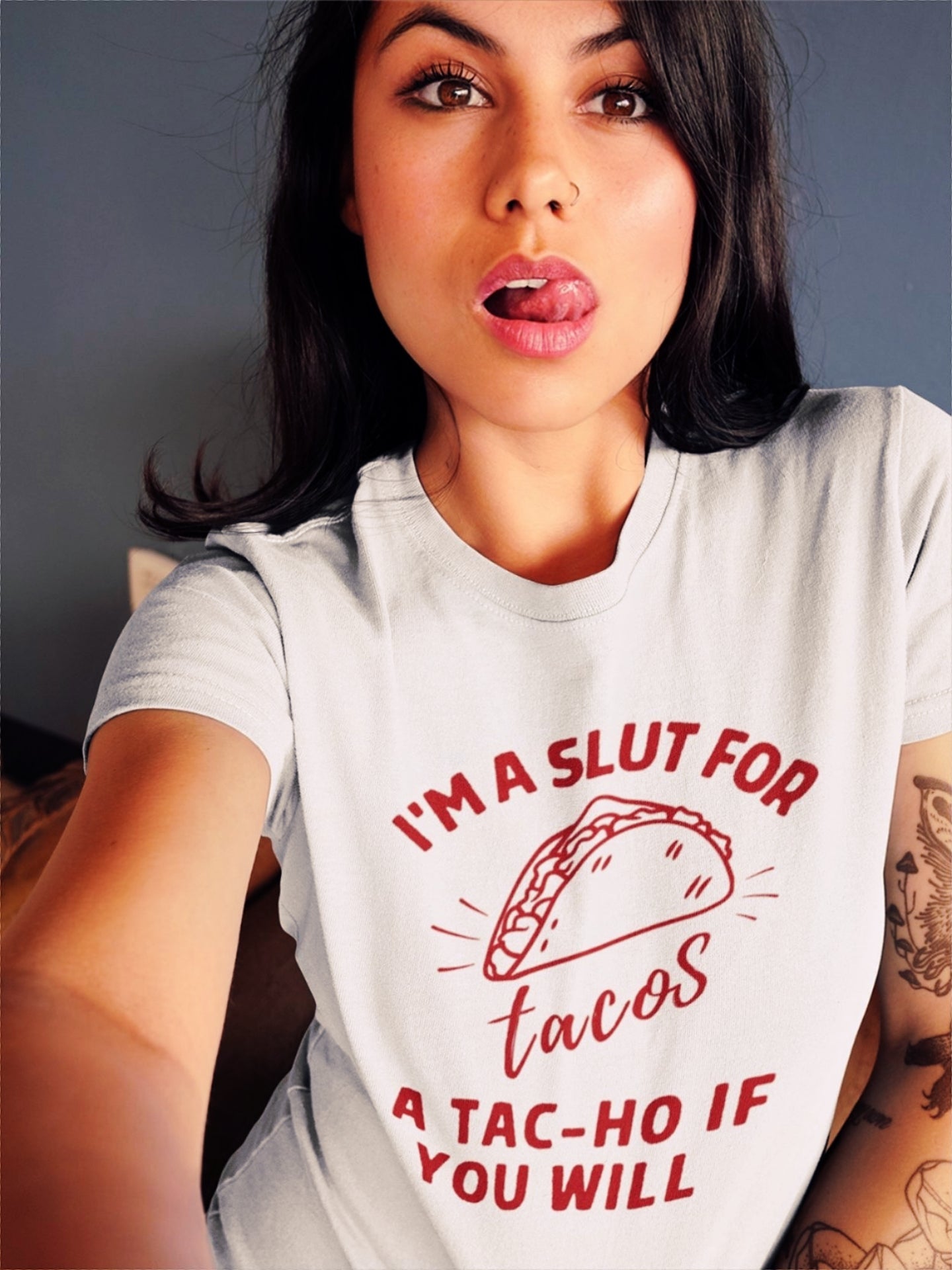 Latina woman wearing a Funny white T-shirt for Latinos, Spanish speakers, and taco lovers. In classic red lettering, the graphic says "I'm a slut for tacos, a tac-ho, if you will". There is also a stylized taco on the shirt