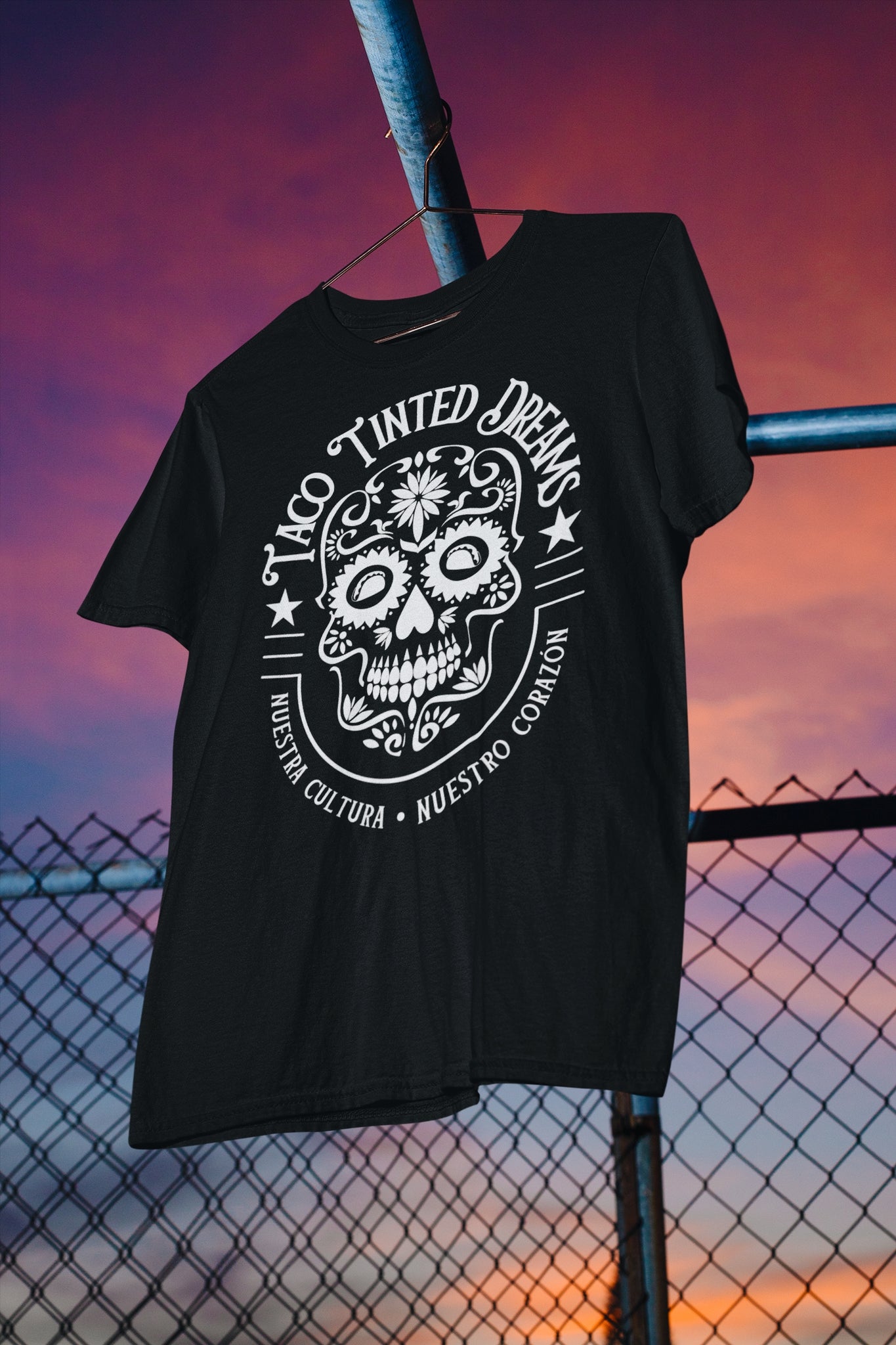 tattoo-style Mexican sugar skull logo with text "taco tinted dreams" and "nuestra cultura, nuestro corazón" on a black t-shirt