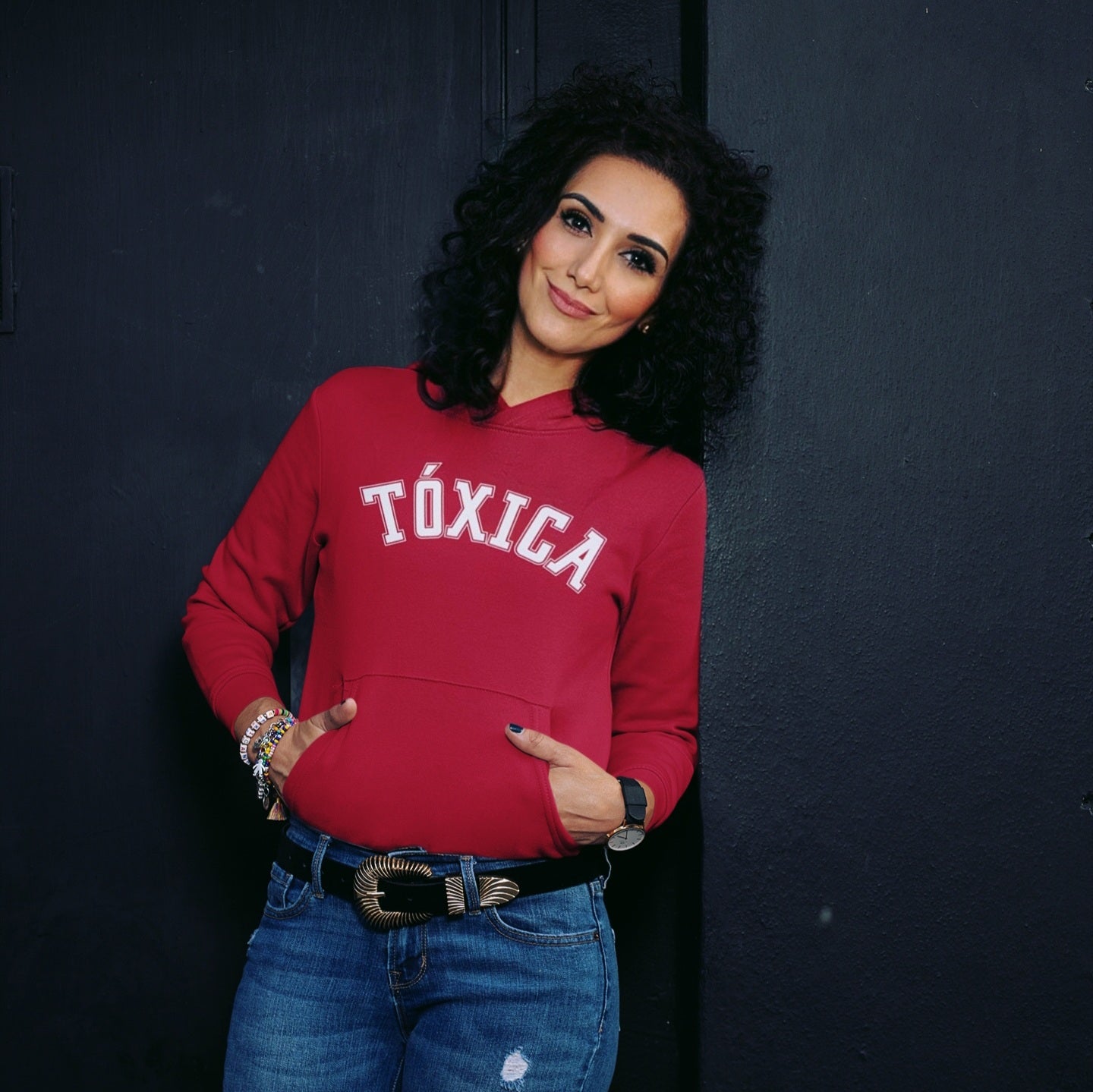 Latina wearing a women's red hoodie sweatshirt with the word 'Toxica' written in white vintage arch-style lettering